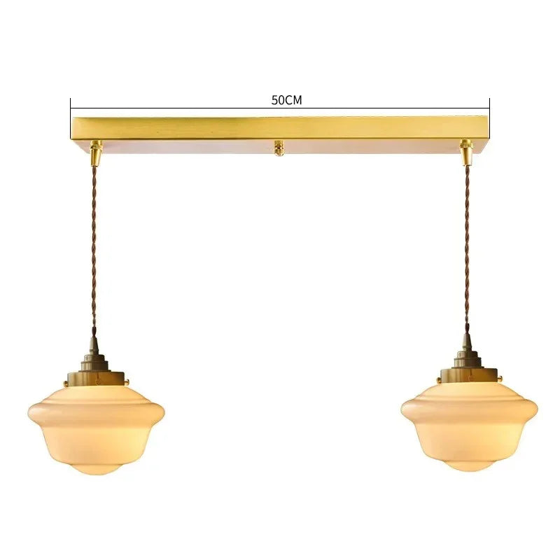 Two opal shades hanging from a brass bar on twisted fabric cords