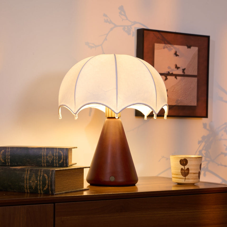 Nightstand lamp lit warm on a dresser beside a patterned cup