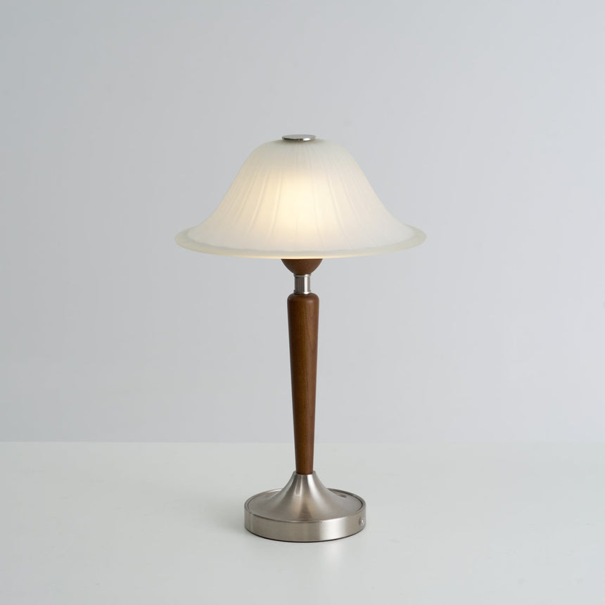 Nightstand table lamp lit and seen in full against a plain ground