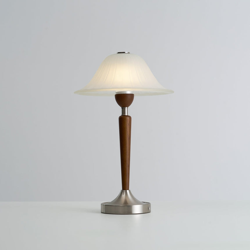 Nightstand table lamp lit in a warm tone against a plain ground