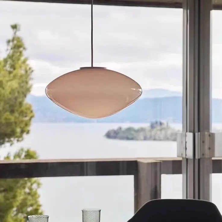 The opal pebble shade lit beside a window looking onto a lake
