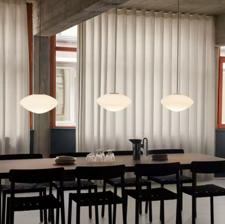 Three pebble shades lit in a row above a long table with black chairs