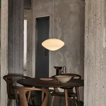 The opal pebble shade lit above a wooden table in a bare room