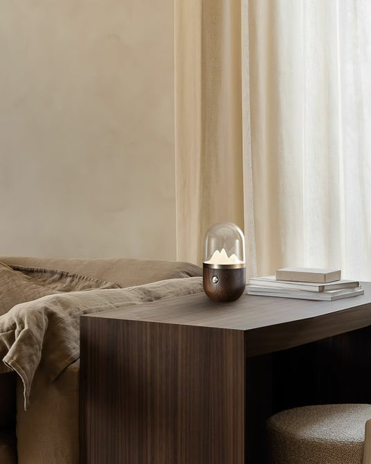 Nursery table lamp lit on a bedside table beside a book and a blanket