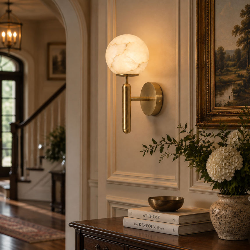 The lit globe on a paneled wall beside a staircase and a vase of stems