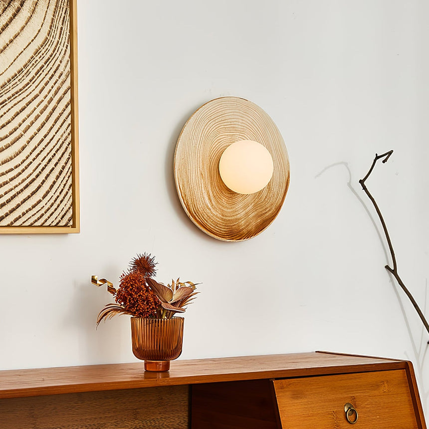 The sconce above a low sideboard beside a bare branch and a small vase