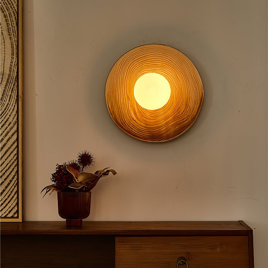 The sconce glowing warm in the evening above a sideboard and dried flowers