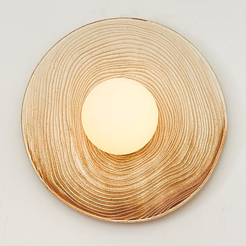 The ringed sconce lit on a pale wall, seen from the front