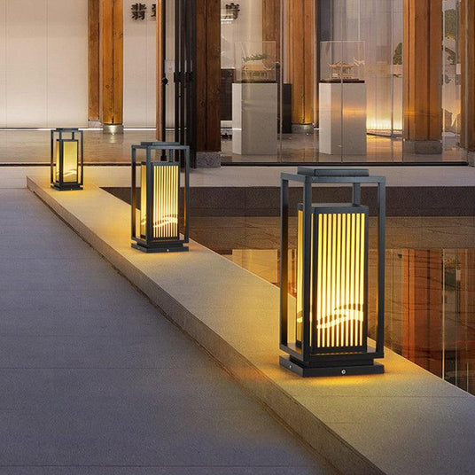 The lantern glowing beside a doorway on a paved terrace in the evening