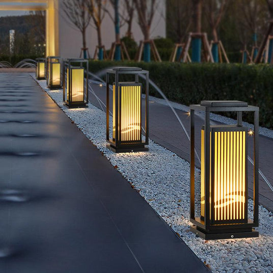 Two cage lanterns lit along a paved path beside low garden planters