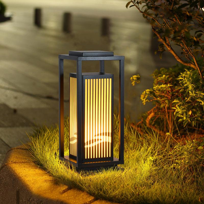 The cage lantern lit among low planting at the edge of a garden path