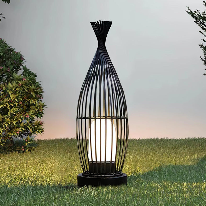 The cage lantern lit on a lawn against a pale evening sky
