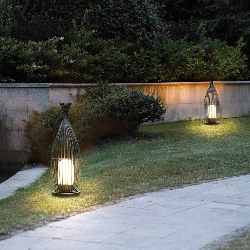 The lantern lit on a lawn beside a clipped hedge and a stone wall