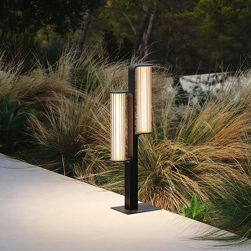 The two arm body lit beside ornamental grasses at a paved path edge