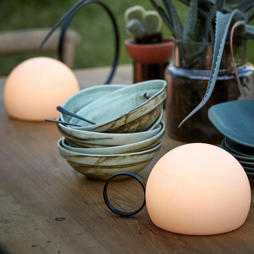Lit on a timber table beside stacked ceramic bowls and a plant