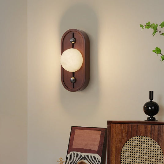 Sconce lit above a console with leaning frames, a cane panel and a plant