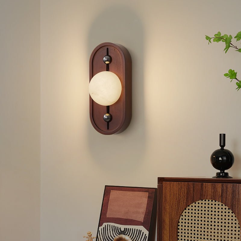 Sconce lit above a console with leaning frames, a cane panel and a plant