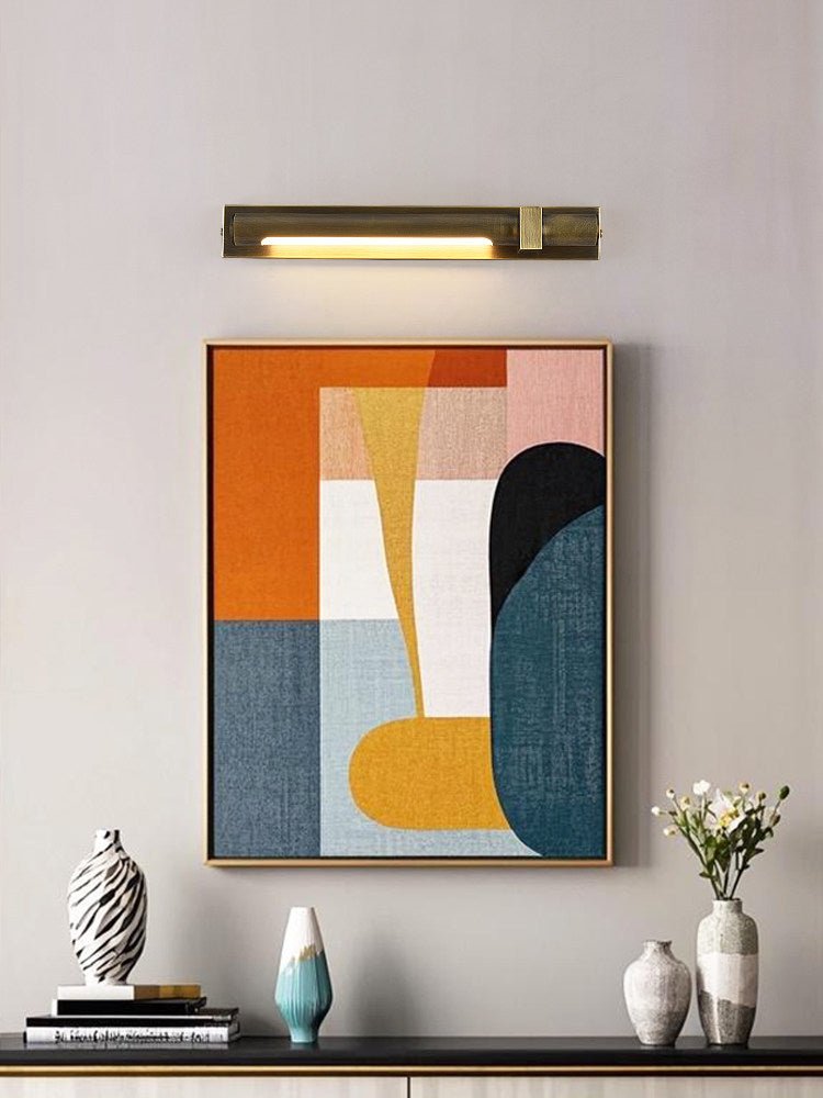 Bronze bar lit over a framed canvas above a console with books and vases