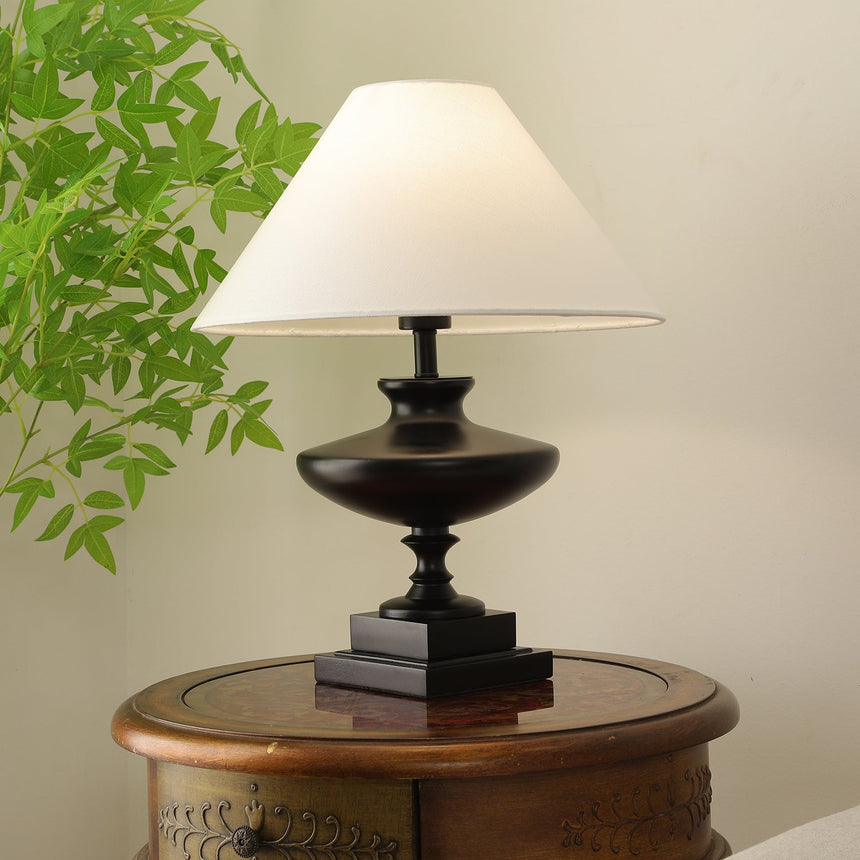 Black oversized table lamp seen from the front, urn base and plinth