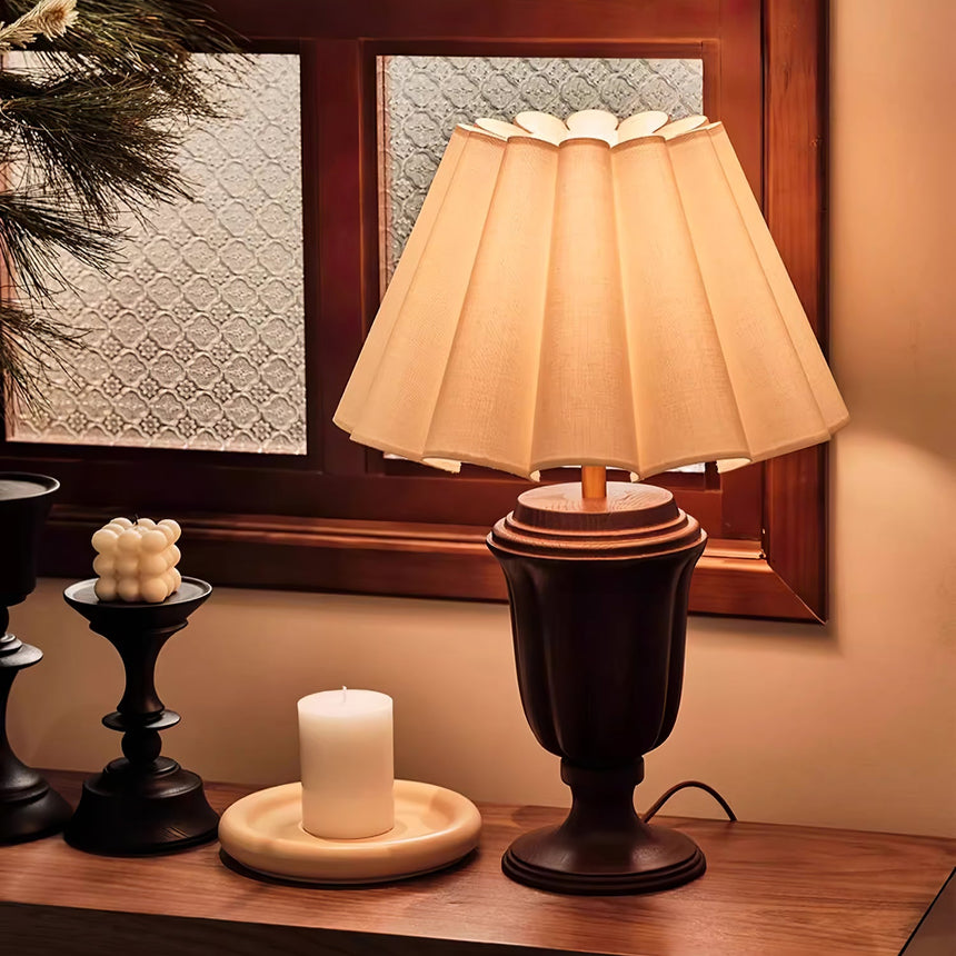 Urn base lamp lit on a sideboard beside a candle on a wood tray