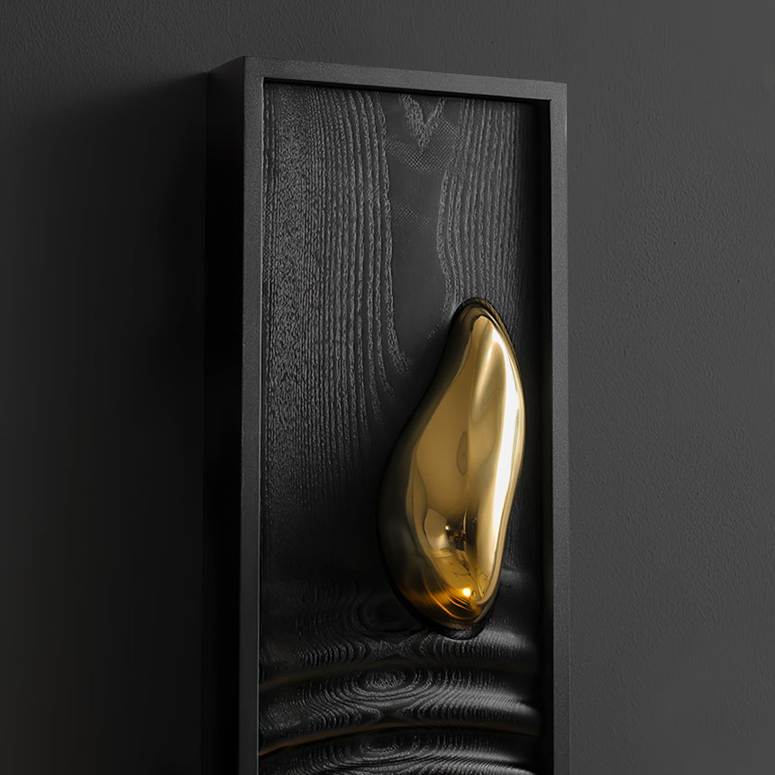 The polished brass teardrop set into the top of the carved wood panel
