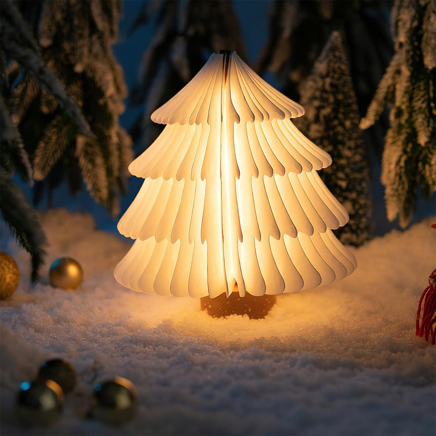 White paper tree lamp lit in a table setting with fake snow and pine