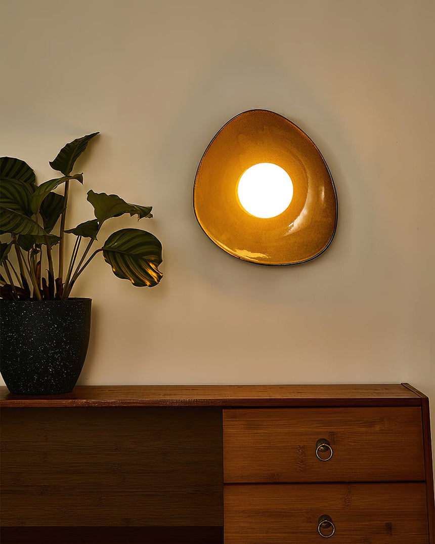 The small pebble light lit warm above a teak sideboard and a plant