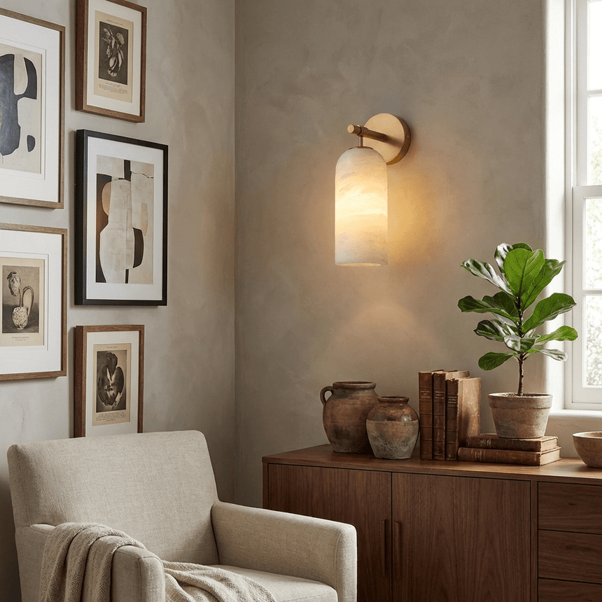 The sconce lit on a gallery wall above a cabinet and a woven armchair