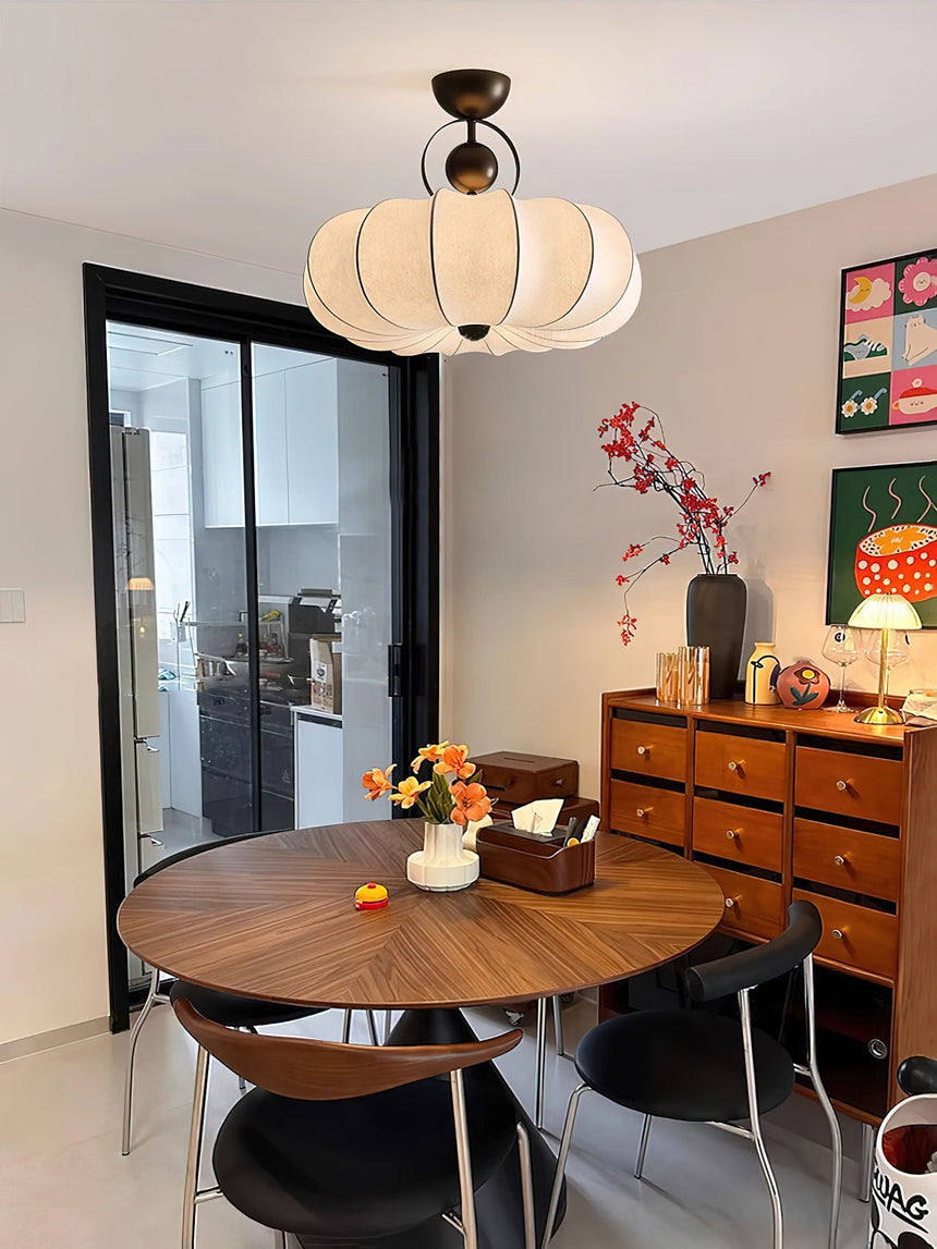 Pleated silk ceiling light over a round wood dining table beside a glass partition