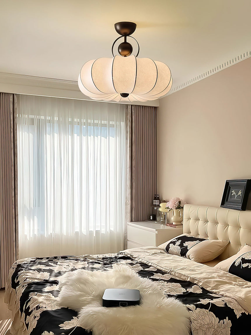 Pleated silk ceiling light above a bed with a tufted headboard and long curtains