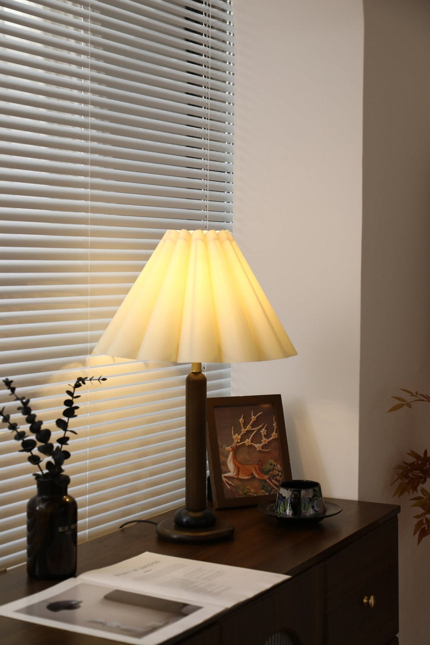 Pleated table lamp lit in a corner beside a framed picture
