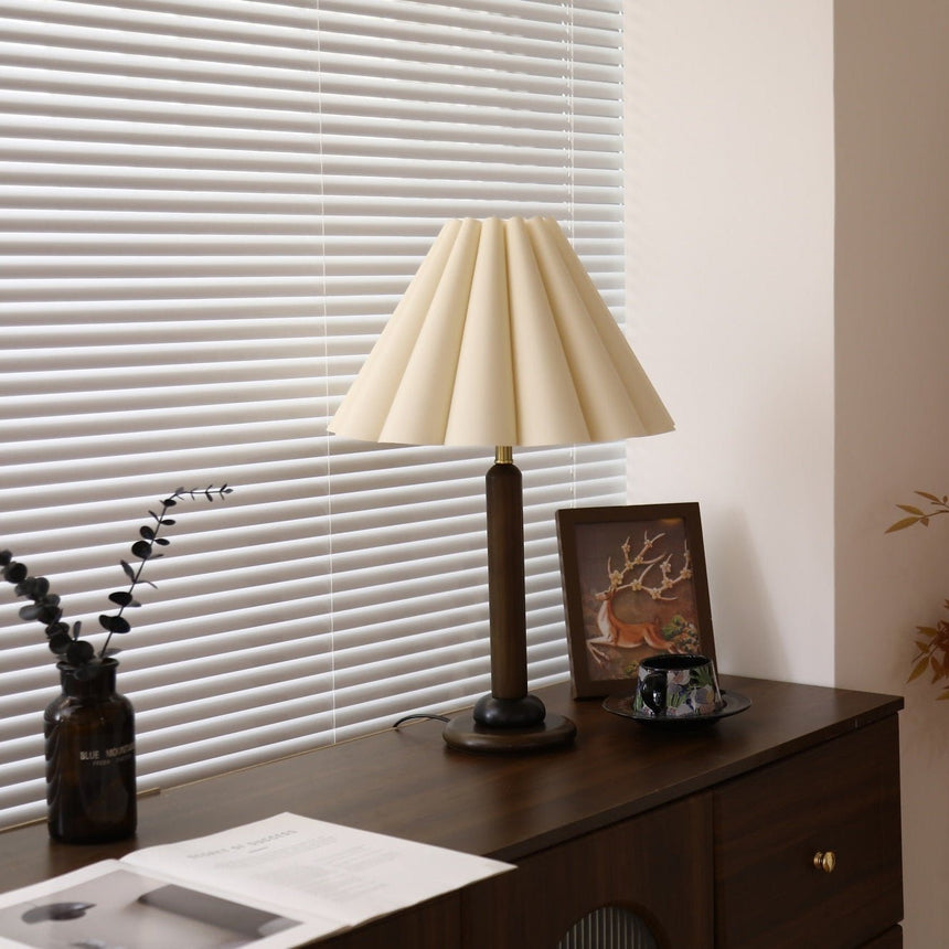 Pleated table lamp lit on a dark dresser beside a framed picture