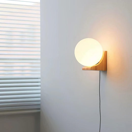 Glass orb sconce lit on a wall beside a window with slatted blinds