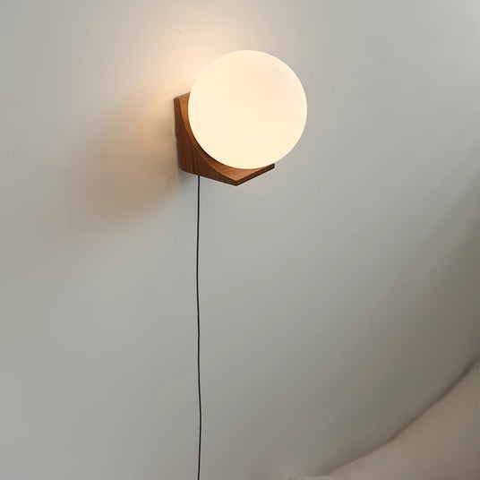 Glass orb sconce lit on a pale wall, the cord running down beside it