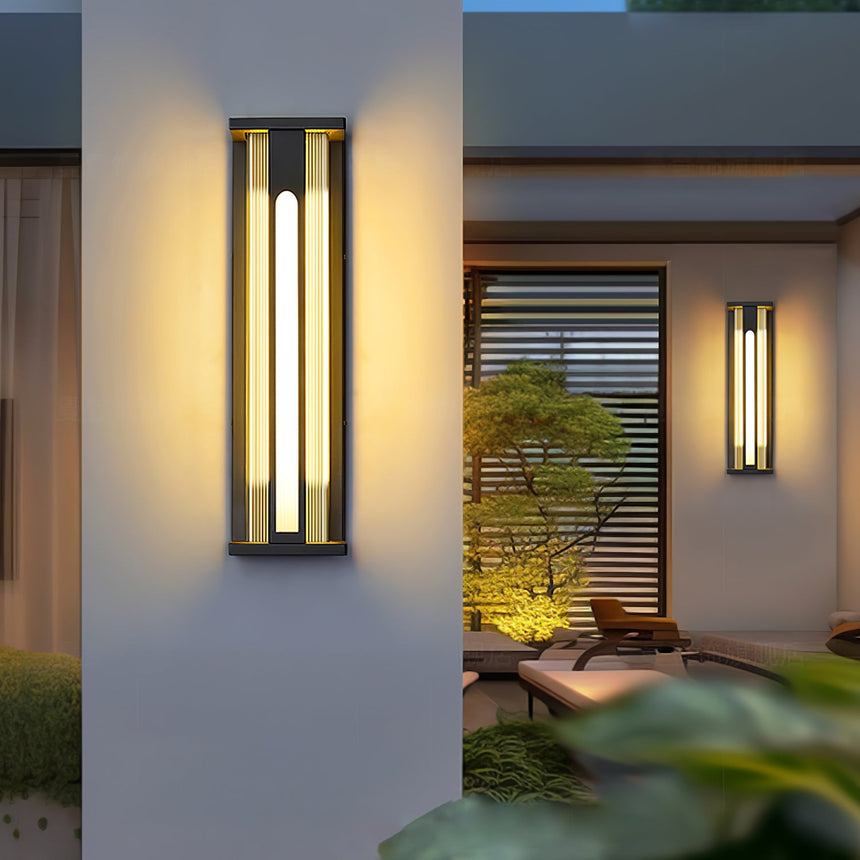 A lantern lit on a garden pillar, a second one on the wall behind the plants