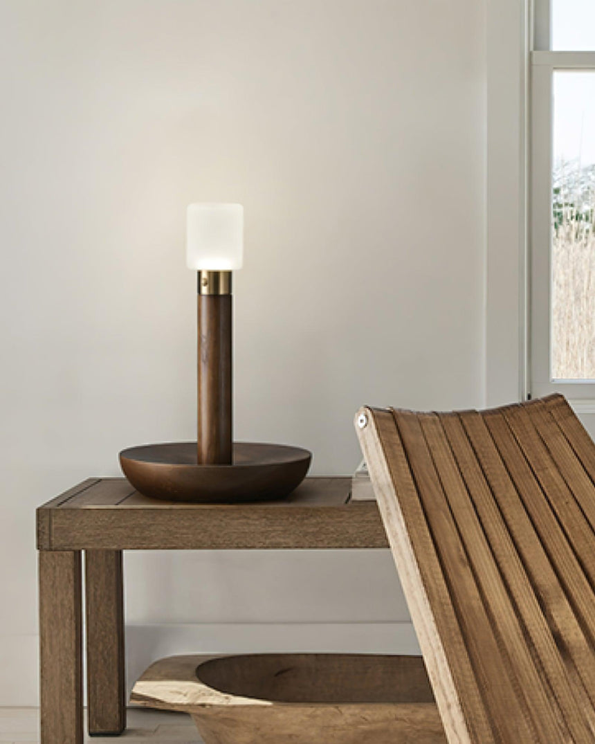 Portable table lamp lit on a wood bench beside a slatted panel