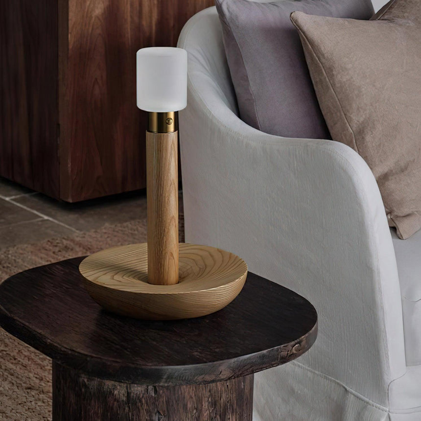 Portable table lamp lit on a round side table next to a pale armchair