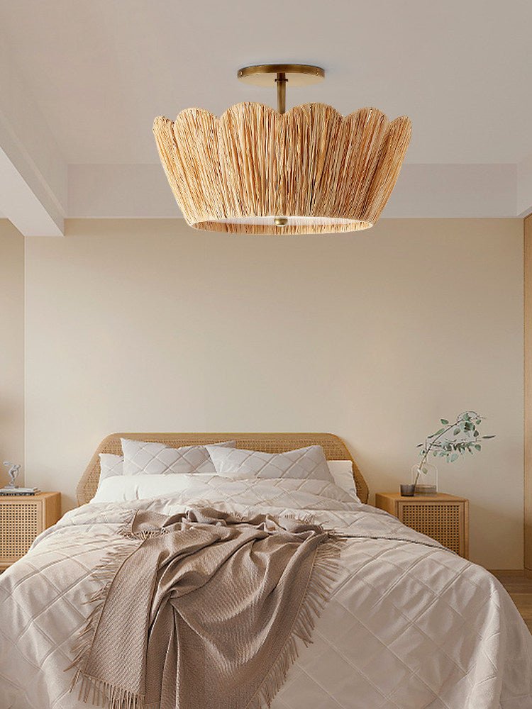 Raffia ceiling light lit over a bed with rumpled linen and a wood headboard