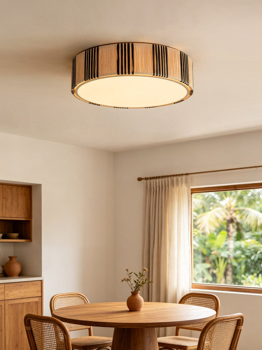 Striped raffia drum ceiling light above a round dining table with wood chairs