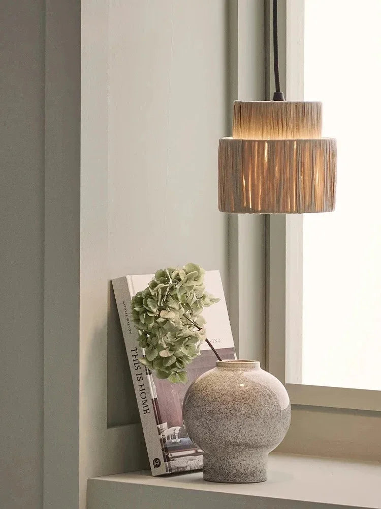 Rattan drum pendant light lit in an interior with a vase