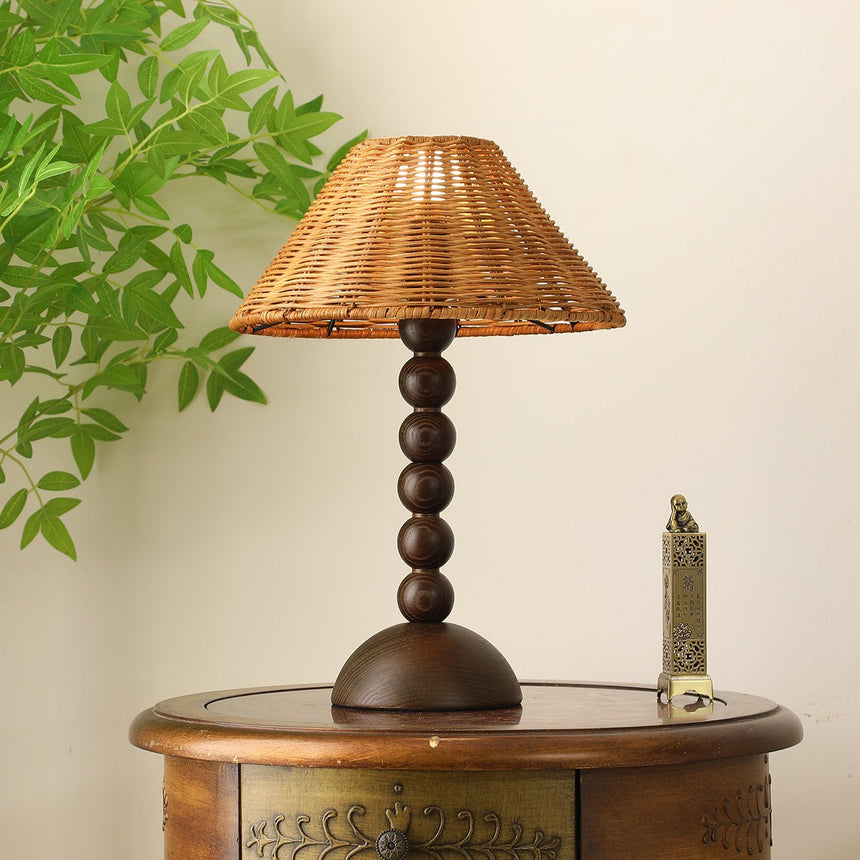 Rattan shade lamp lit on a round painted table beside a green plant