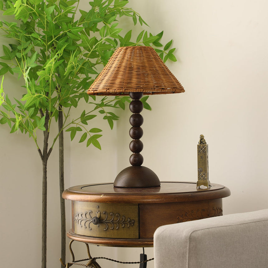Rattan shade lamp lit warm against a pale wall beside a plant