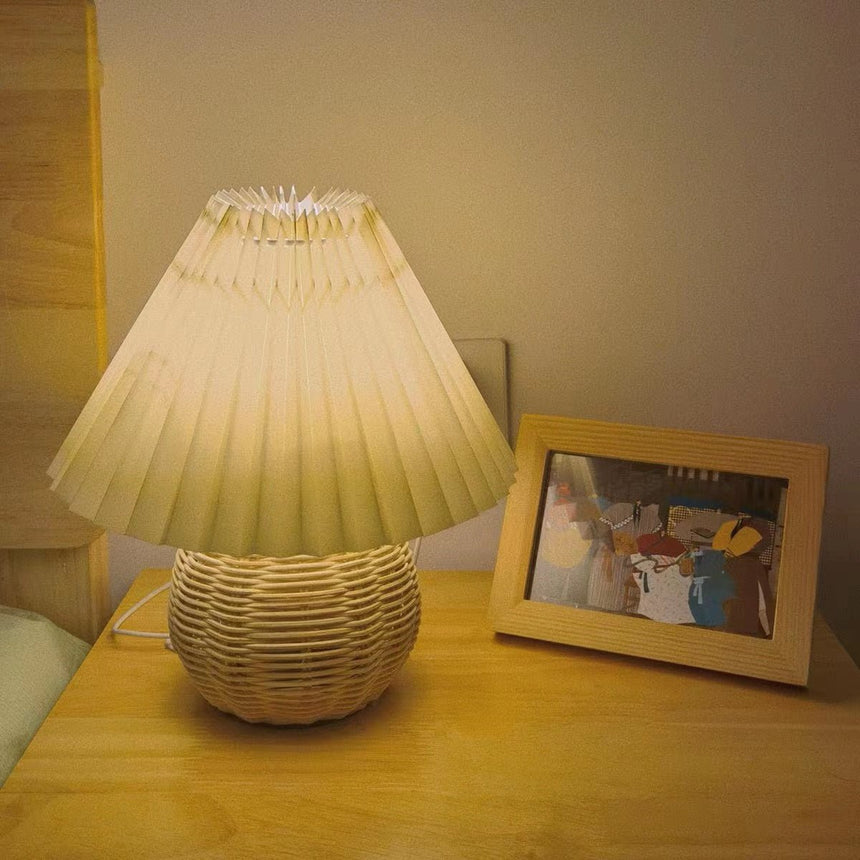 Rattan table lamp lit on a wooden surface beside a framed photograph