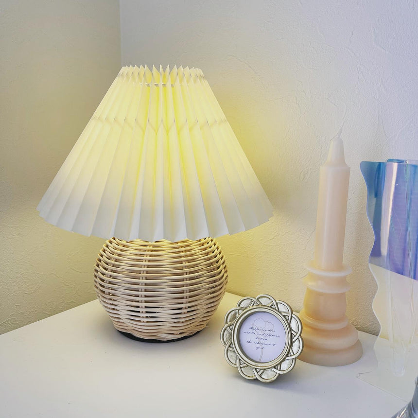 Rattan table lamp lit in a corner beside a candle and a photo frame