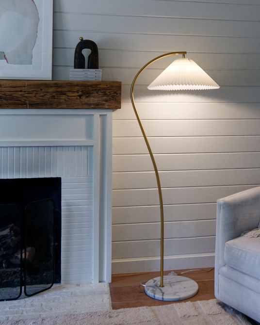 The curved brass lamp lit beside a white fireplace, a mantel and a gray sofa