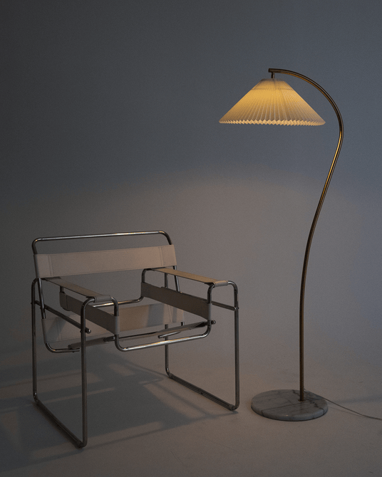 The lamp lit above a chrome and leather chair against a dark gray wall