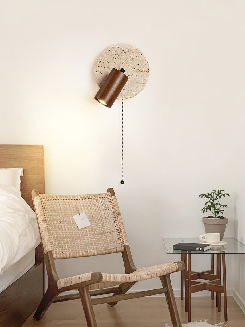 Sconce lit beside a cane chair and a side table holding a small plant