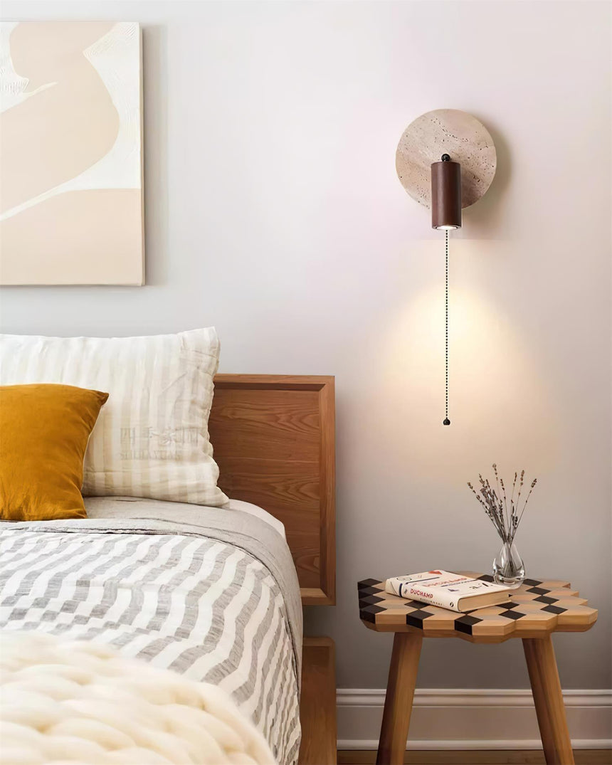 Sconce lit beside a bed with striped cushions and a stool of stacked books