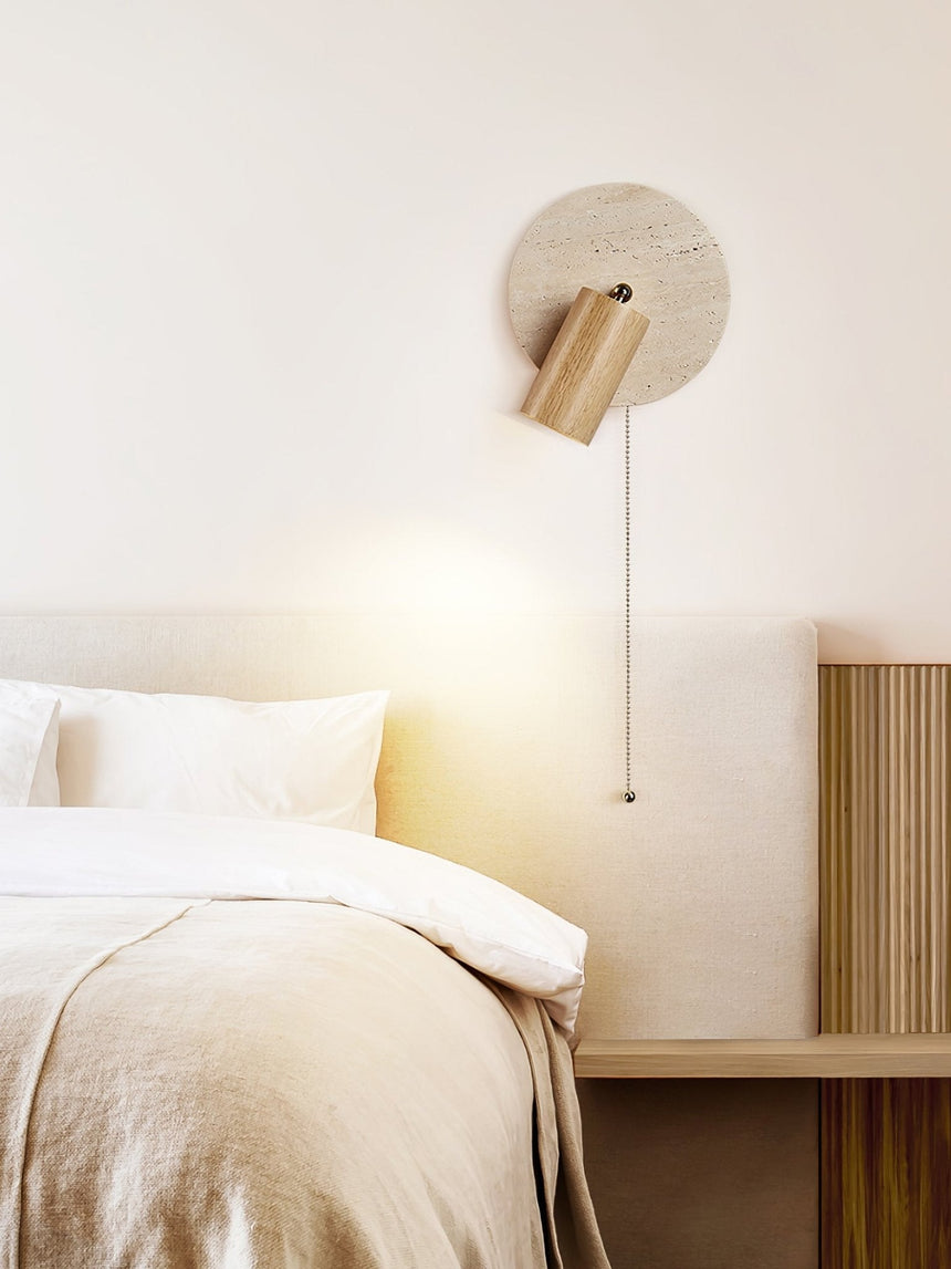 Sconce lit on a wood panel wall above a bed with a folded throw