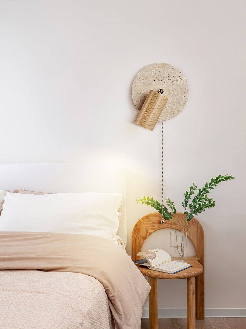 Sconce lit beside a bed above a cane nightstand holding a potted fern